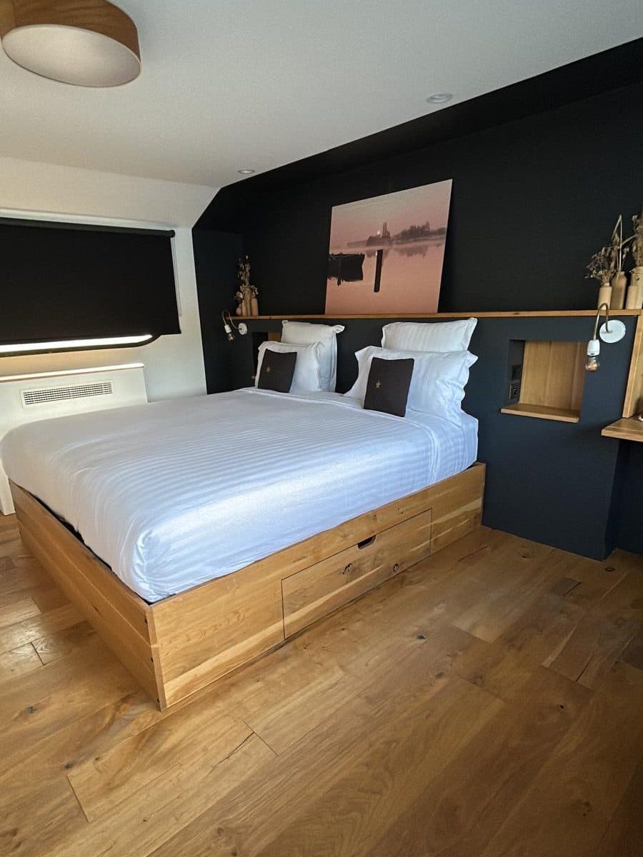 Chambre au lit fait de linge blanc, tableau au-dessus du lit