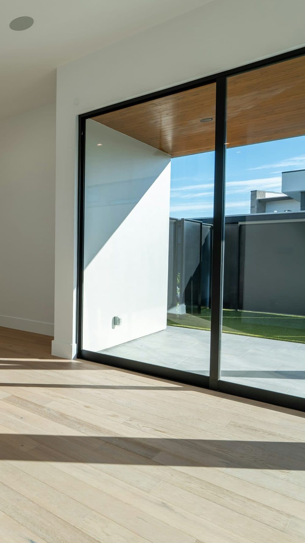 Pièce claire et vide au parquet clair, baie vitrée ouverte sur une terrasse
