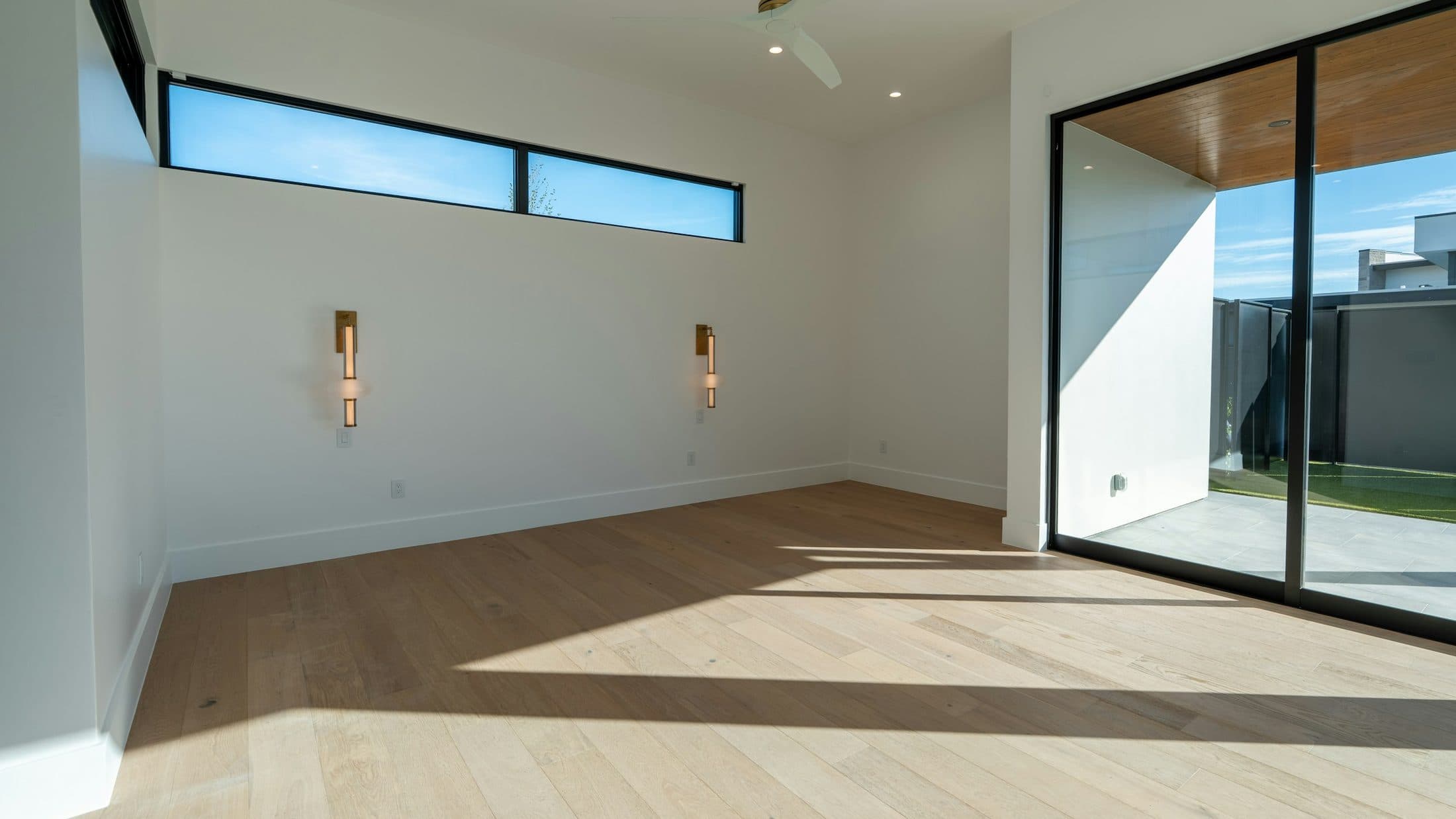 Pièce claire et vide au parquet clair, baie vitrée ouverte sur une terrasse